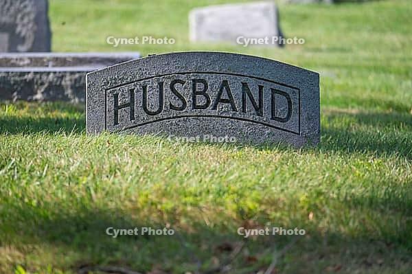 Antique grave stone reads husband in tranquil green grass cemetery with sunshine and dappled sunlight. Large letters are readable. No people with copy space [IBR125557562]