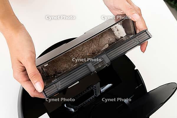 Robot vacuum cleaner in female hands. Woman takes out container and filter to clean it from dirt and debris. Concept of cleaning with cordless vacuum cleaner, close-up [IBR125557579]