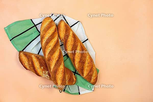 Three freshly baked traditional baguettes on the background of the color of powder with copy space. Top view, flat lay. French cuisine [IBR125557585]