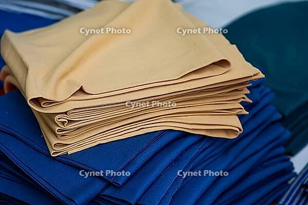 Beige folded clothes neatly stacked atop vibrant blue fabrics, showcasing an organized arrangement typical of a textile factory or warehouse setting [IBR125557590]