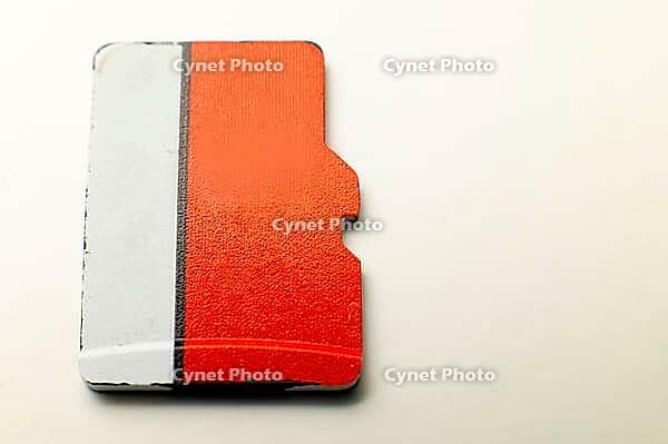 Top view of unrecognizable red and white micro sd flash drive on white background. Used flash drive with scuffs concept of old storage media [IBR125557620]