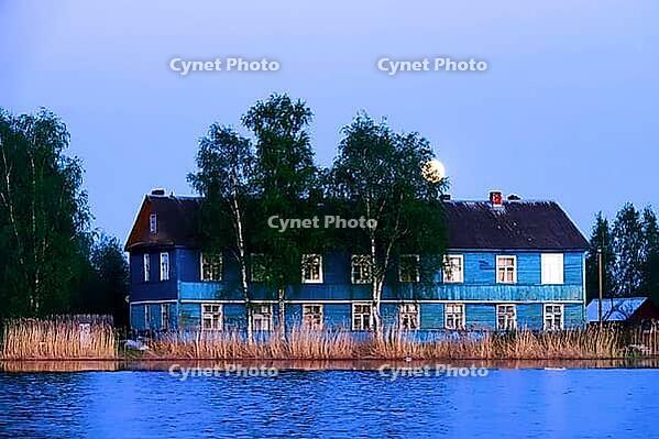 The full-orbed moon rises over the spring river, forest and village during the daytime, quiet evening romantic nature. Two-storey old wooden house on the river bank [IBR125565994]