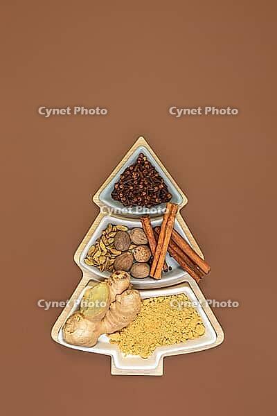 Cloves, cinnamon, nutmeg, cardamom and ginger for making ginger cookies in a box in the shape of a Christmas tree on a brown background with copy space. Concept of festive Christmas baking. Top view, flat lay [IBR125566003]