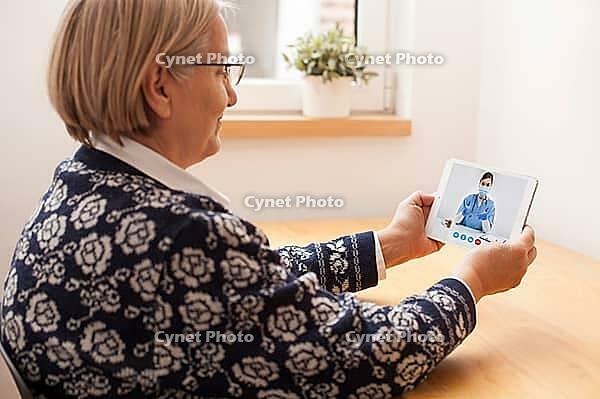 Reindeer elderly senior woman talking to GP doctor about virtual telemedicine video call, holding tablet computer, female doctor giving consultation over laptop computer screen, remote appointment at home [IBR125566040]