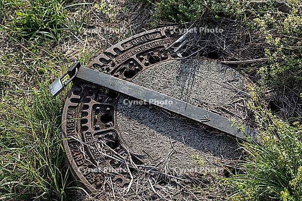 07 October 2026, A rusty metal manhole cover is secured with a steel bar and padlock in a grassy field [IBR125566053]