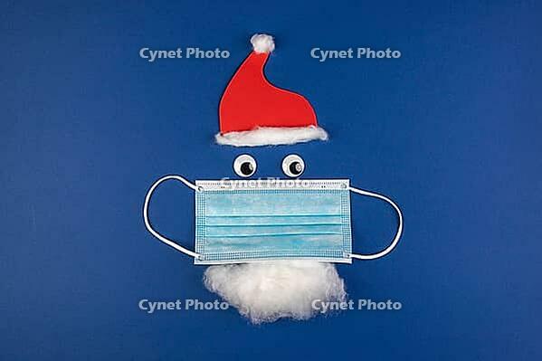 Handmade Santa Claus with moth protection, face mask, red cap and beard, as a symbol of effects in covid virus during Christmas season, blue background [IBR125566073]