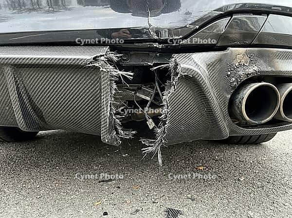 Fractured composite panels hang beneath the rear bumper, revealing wiring and underbody parts beside metal exhaust outlets above the pavement, AI generated [IBR125592656]