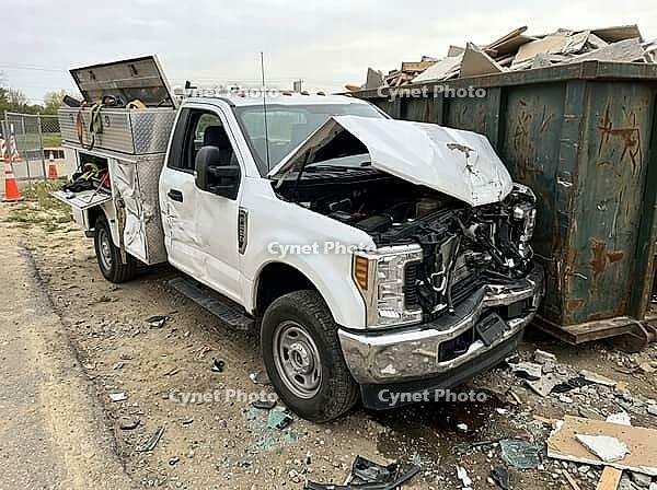 A white utility pickup sits amid broken glass and rubble, its hood bent upward beside a metal container filled with demolition waste at a work site, AI generated [IBR125592668]