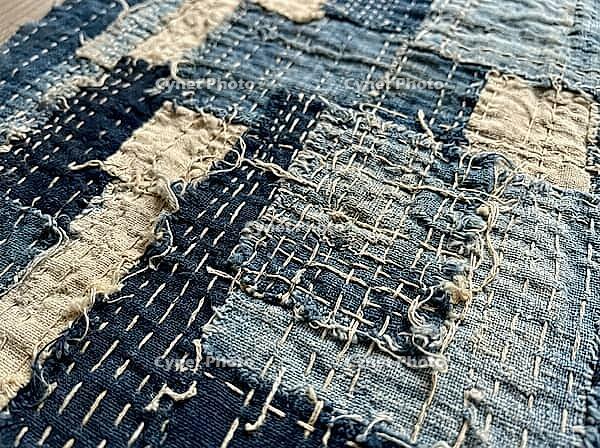 Layered cotton patches, frayed edges, and irregular hand stitching reveal the coarse weave of a timeworn blue-and-cream textile in close detail, AI generated [IBR125592683]