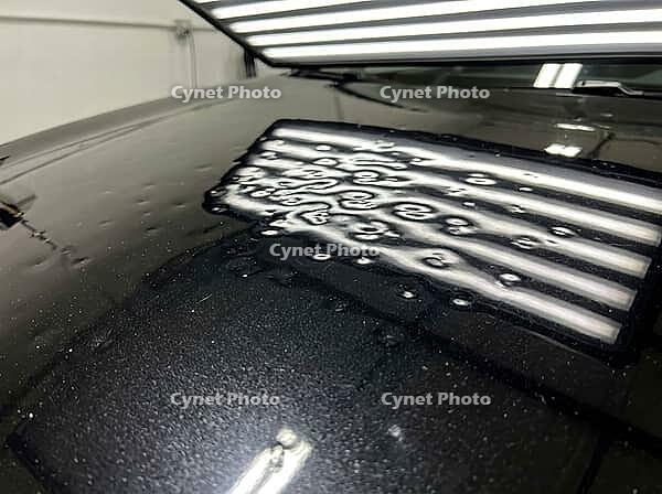 Black car hood displays multiple dents from hail, clearly visible under professional light bars, indicating severe damage needing expert paintless dent repair and auto body restoration, AI generated [IBR125592697]