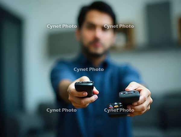 Man fighting to operate television, holding multiple remote controls with a confused expression, AI generated [IBR125592699]