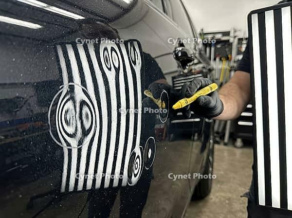 A gloved hand uses a yellow marker beside reflected inspection lines to locate panel damage in a professional auto body repair workshop setting, AI generated [IBR125592721]