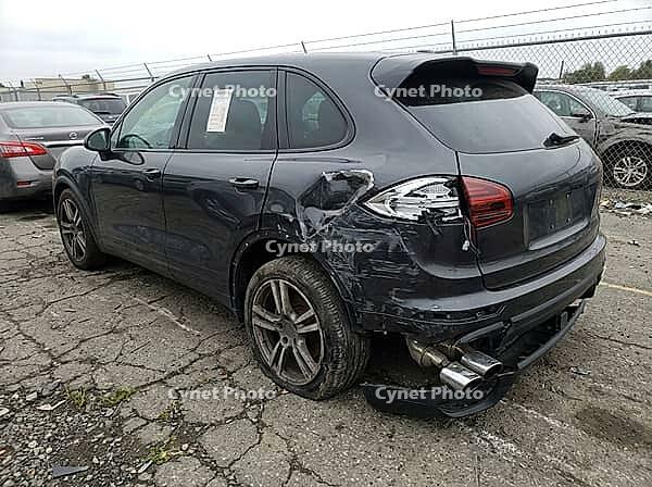 Parked among other vehicles on cracked pavement, the dark crossover shows torn bodywork, a damaged rear bumper, exposed exhaust tips, and a window tag, AI generated [IBR125592723]