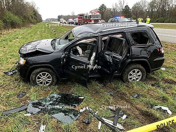 Shattered glass and vehicle debris cover the grassy shoulder while a fire engine and flashing emergency lights appear along the road nearby, AI generated [IBR125592730]