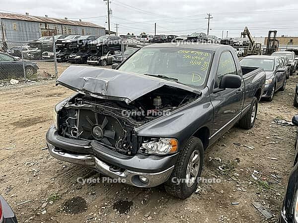 Gray pickup truck displaying severe front end damage from a collision, parked in an outdoor salvage yard surrounded by other derelict vehicles awaiting dismantling and recycling, AI generated [IBR125592733]