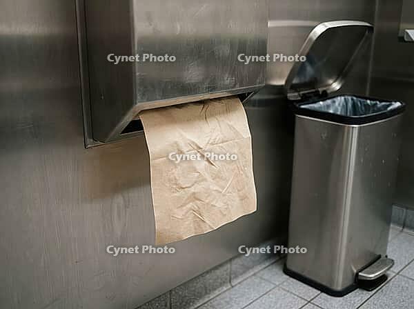 Brown paper towel hangs from a stainless wall dispenser beside an open pedal bin, showing a simple setup for hand drying and waste disposal, AI generated [IBR125592747]