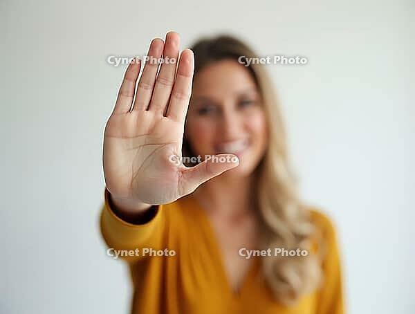 Smiling woman showing stop gesture with hand in bright studio setting, AI generated [IBR125621287]