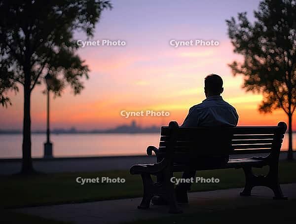 Person sitting on a bench, gazing at the sunset over calm waters, AI generated [IBR125621311]
