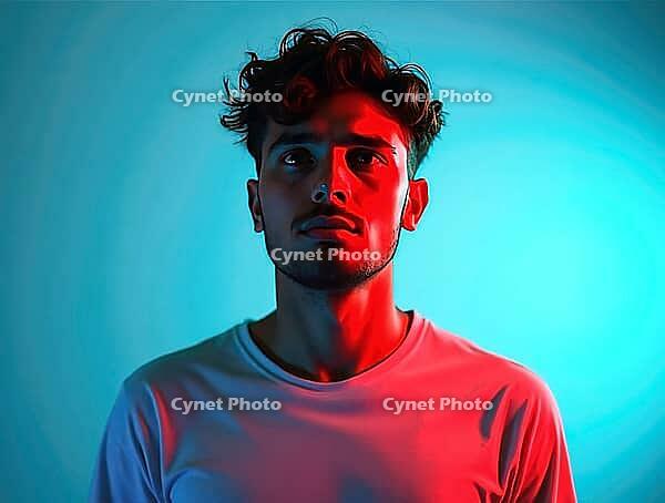 Studio portrait of a thoughtful young man with curly hair, illuminated by contrasting red and blue neon lights, creating a dramatic and colorful atmosphere, AI generated [IBR125621319]