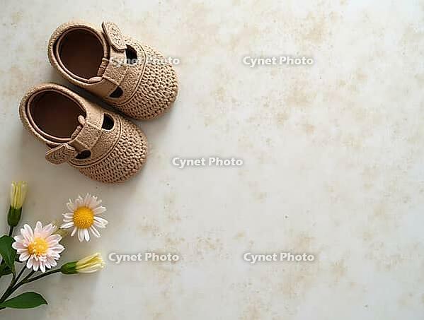 Small crocheted baby shoes and daisies are displayed on a marble countertop, creating a serene and minimalist composition, AI generated [IBR125621349]