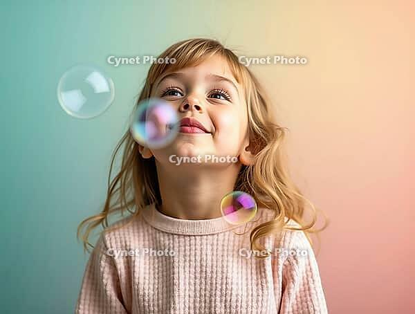 Portrait of a cheerful little girl blowing soap bubbles with a joyful expression on her face, against a pastel-colored studio backdrop, AI generated [IBR125621367]