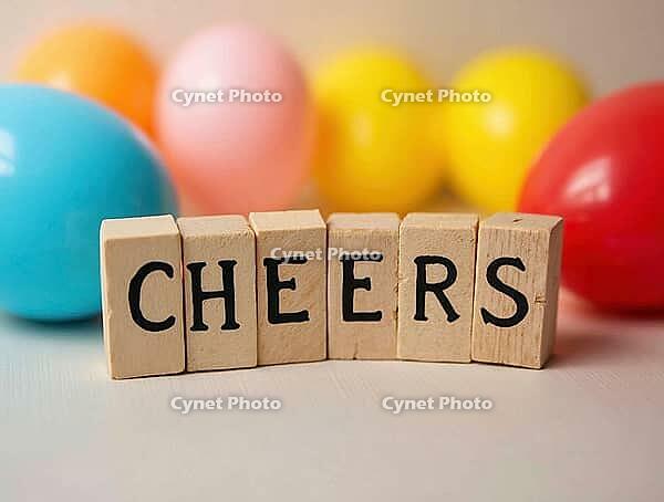 Wooden cubes spelling cheers with colorful balloons blurred in the background, creating a festive atmosphere, AI generated [IBR125636882]