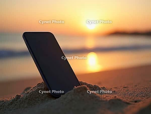 Mobile phone standing in the sand with ocean waves and sunset bokeh in the background, AI generated [IBR125636920]