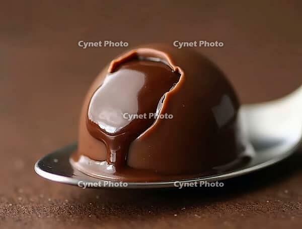 Cracked chocolate praline on spoon, revealing rich ganache filling, tempting indulgence, AI generated [IBR125636921]