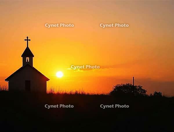 Serene countryside church stands silhouetted against a vibrant sunrise, its cross reaching towards the golden sky, AI generated [IBR125636927]