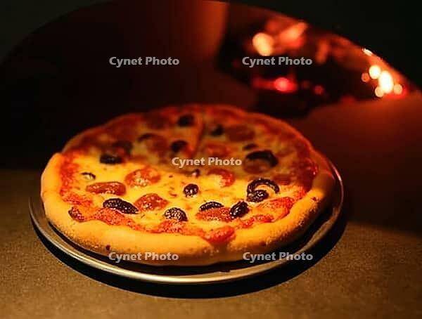 Freshly baked pizza with pepperoni and black olives coming out of a traditional wood-fired oven, AI generated [IBR125636930]