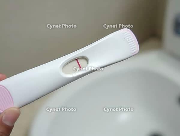 Positive pregnancy test result is held by a hand in a bathroom setting, AI generated [IBR125636938]