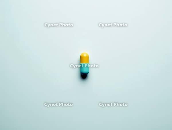 Yellow and light blue capsule resting on a sterile white surface, representing medication, healthcare, and pharmaceutical concepts, AI generated [IBR125636957]