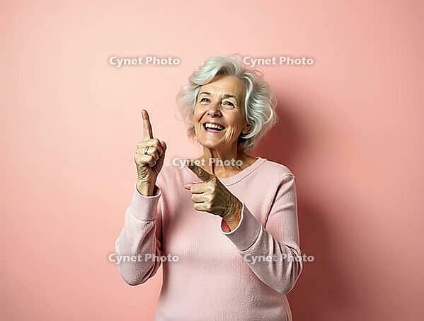 Studio portrait of cheerful elderly woman pointing up and showing something with index fingers on pink background, AI generated [IBR125653407]