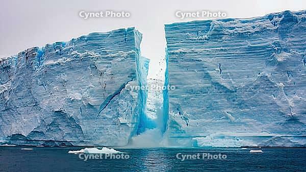 Ice crashing down from a massive iceberg into the deep blue ocean of Antarctica, forming a striking, jagged crack in the ice, AI generated [IBR125653458]