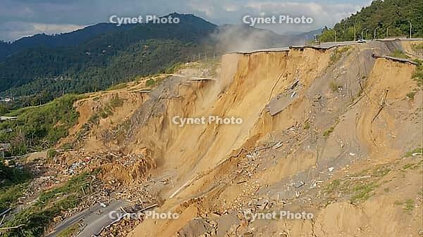 Landslide destroying asphalt road in mountain area creating deep chasm, causing traffic disruption and infrastructure damage, AI generated [IBR125653459]