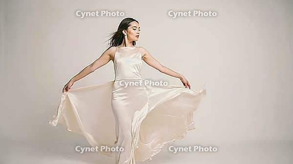 Fashion model dancing gracefully in an elegant long beige dress, showcasing beauty and style against a clean white studio background, AI generated [IBR125653470]