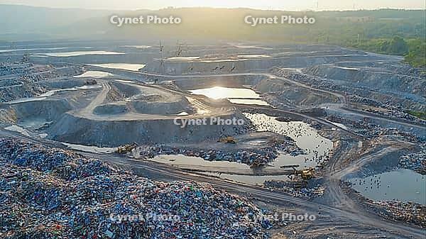 Aerial view capturing a vast landfill with bulldozers working diligently while birds soar overhead against a vibrant sunset backdrop, AI generated [IBR125653482]
