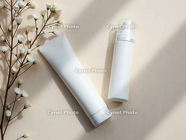 White cosmetic containers lying on beige table near flowers under sunlight, creating wellness and self-care atmosphere, AI generated [IBR125653494]