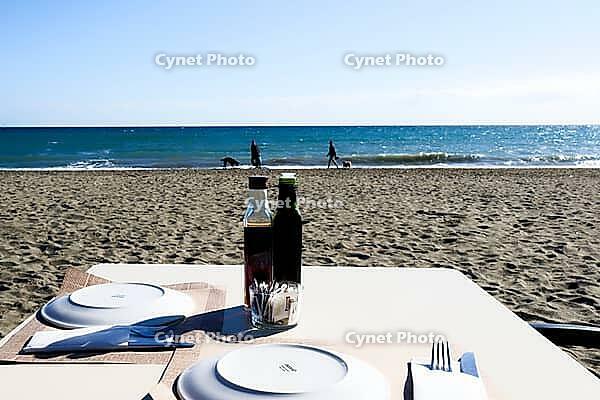 A covered restaurant table stands on the sunny sandy beach overlooking the sea, Estepona, Costa del Sol, Andalusia, Malaga province, Spain [IBR125657385]