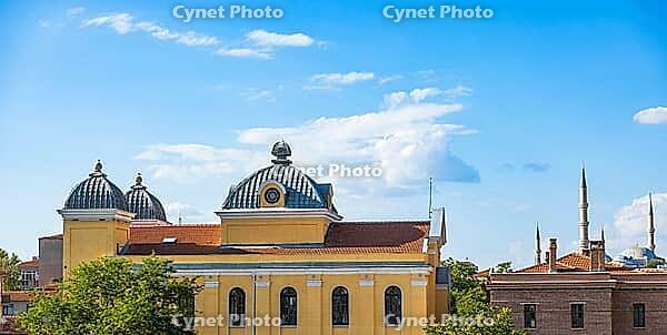 A yellow historic building with patterned domes stands among trees beneath a bright blue sky, with mosque minarets visible in the distance [IBR125657404]