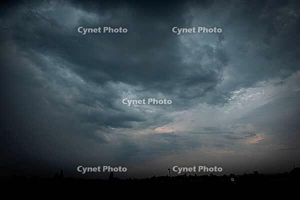 Dark storm clouds sweep across the sky above a nearly black distant landscape, with faint warm light near the horizon - Czech republic [IBR125657428]