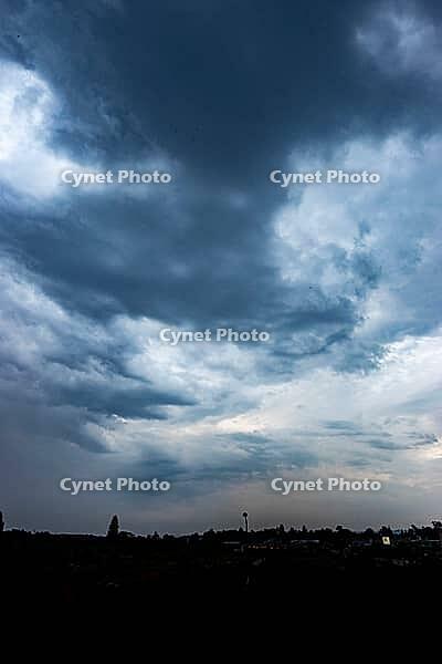 Heavy blue-gray storm clouds loom over a distant town silhouetted along the horizon - Czech republic [IBR125657437]